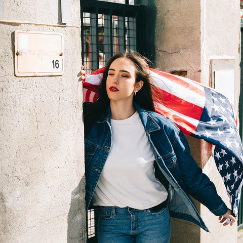 Woman in denim jacket posing with American flag against rustic stone wall